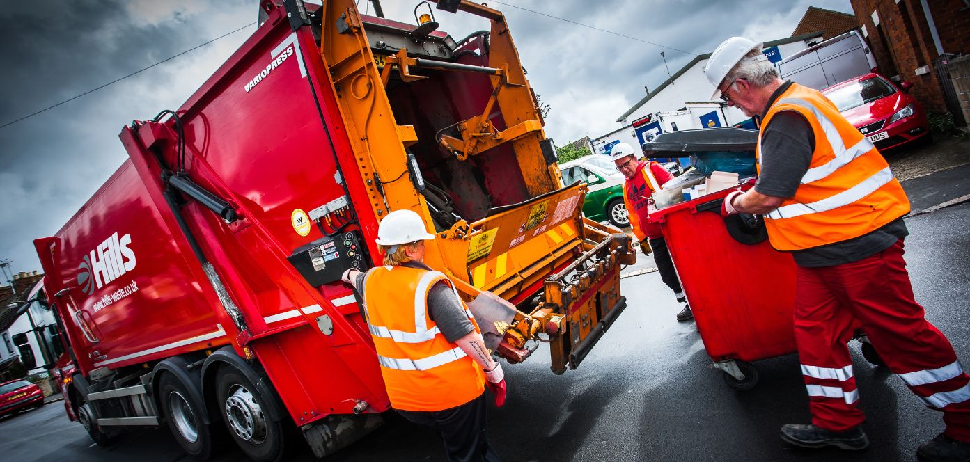 Waste collection team operating near a refuse truck while using software-supported workflow on a residential street