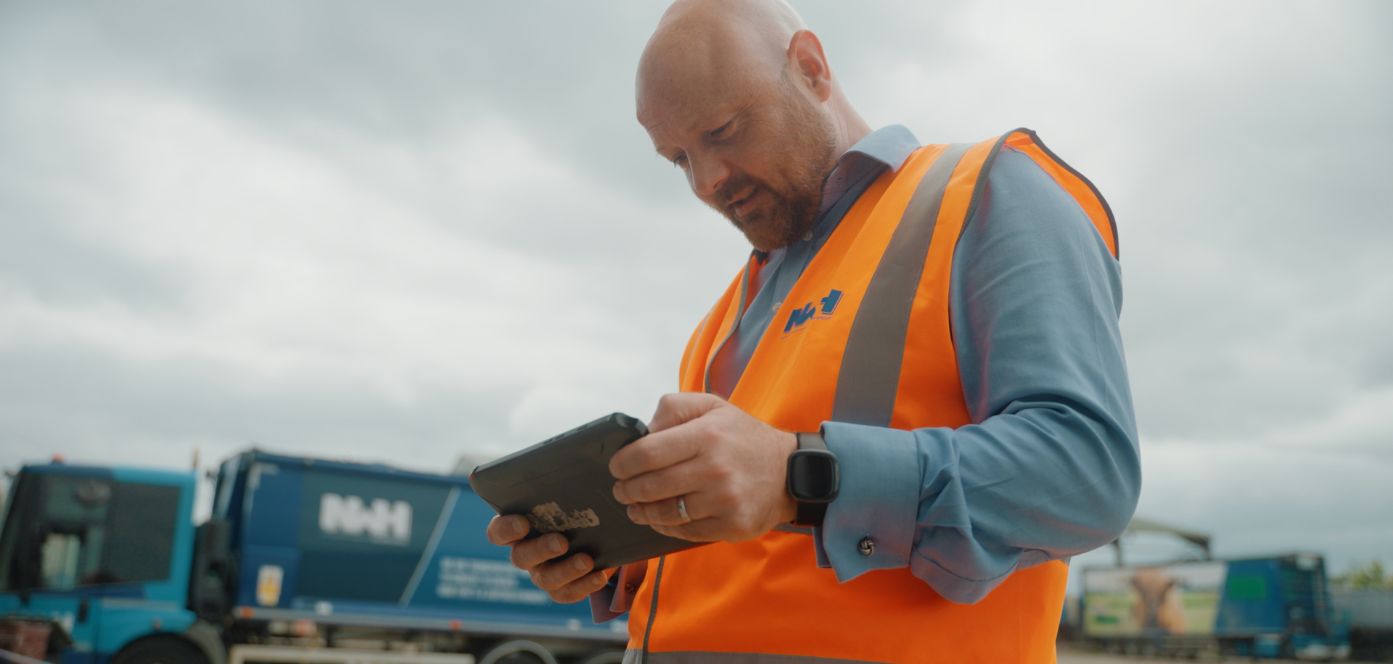 Waste site operator using a tablet device to access weighbridge software with trucks in the background